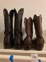 Rear view of two pairs of Lucchese cowboy boots, one black and one brown, showing the back detail and heel wear.