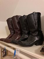 Two pairs of Lucchese cowboy boots shown together side by side on a shelf, one black pair and one brown pair, both size 10.5.