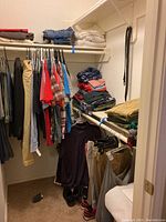Closet view showing hanging shirts, pants, and folded clothes on shelves with shoes below