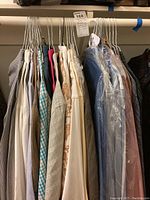 Photo showing 12 men's long sleeve shirts on hangers, some with plastic covers, in various colors and patterns, hung on a metal rod.
