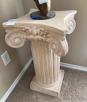 Front angled view of the column pedestal showing carved volute scrolls and fluted vertical grooves with chip damage on base corner.