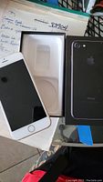 Apple iPhone 7 black color with home button, screen visible, and its original box which is black in color.