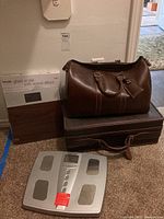 Photo showing Beurer glass scale box with wood effect, two brown carry-on size bags stacked, and Health o meter digital bathroom scale.