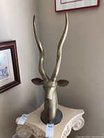 Overall view of brass axis deer head sculpture standing on pedestal, showing height and antlers.