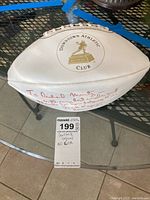 Photo showing white football with Downtown Athletic Club gold logo and handwritten red signature on one side.