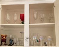 Shelf showing various clear and colored stemware glasses including red goblet and clear tall wine glasses