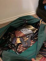 Green carrying bag filled with assorted men's ties showing various patterns including paisley and geometric.