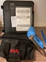Blue Skil electric sander with black carrying bag and hard case marked with instruction manual, all placed on carpet.