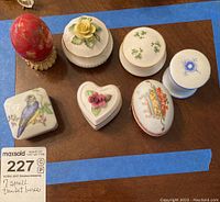 Seven small trinket boxes of different shapes and designs shown on wooden surface