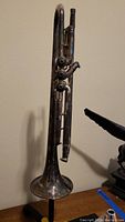 Full side view of a vintage silver trumpet showing three valves and visible wear/tarnish.