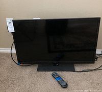 Front angled view of 32 inch Insignia TV and remote control placed in front on carpeted floor.