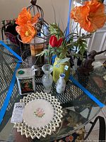 Lot with faux flowers in vases, decorative lace plate, bird cage candle holder, and bird figurine on glass table.