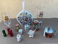 Photo showing various German branded small glasses, ceramic miniature mugs, a large blue and white ceramic vase, and a small brass pot
