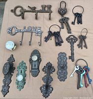 Overhead shot showing the full assortment of key themed decorative items along with vintage door knobs and key ring sets arranged on tan surface.