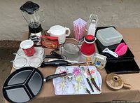 Full view of all 27 kitchen items including blender, divided pans, storage containers, utensils and more arranged on a table.