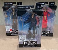 Three unopened action figures from The Princess Bride featuring Inigo Montoya, Dread Pirate Roberts, and Princess Buttercup in black windowed boxes.