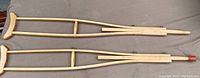 Pair of vintage wooden crutches laid side by side showing full length and overall condition including one with rubber foot missing.