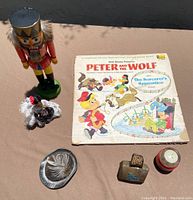 Full photo of the lot including wooden nutcracker, Peter and the Wolf record, Mexican doll, German alpine hat, copper bell, bicycle compass, toiletries bag.