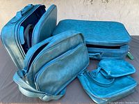 Shows the vintage blue suitcase alongside a matching blue shoulder bag, a blue pouch with snap closure, and a small zippered pouch. All items share the same color and texture.