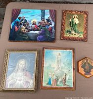 Top view of six framed religious prints arranged on a table showing depictions of The Last Supper, Saint Jude, Sacred Heart of Jesus, Our Lady of Fatima, Virgin Mary, and wood plaque of The Ten Commandments.