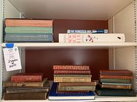 Two shelves of books featuring various titles, some old and fragile, including several leather-bound volumes and boxed sports story collections.