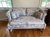 Full view of the loveseat showing the upholstery pattern, overall size, shape and presence of two throw pillows.