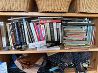 Shelf filled with books including adult biographies, guides, and a stack of children's vintage books, with assorted small office items and jewelry on shelf