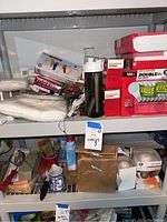 Shelf with new boxed Sylvania DoubleLife 100W lightbulbs packaged in red and white boxes, white vinyl gloves, Camelback water bottle, and assorted crafting materials including brushes, tape, and extension cords.