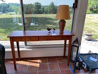 Full view of the wood console/side table with a lamp and two bird figurines on top, near a window.