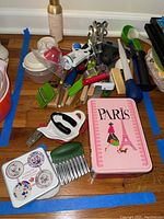 Photo of assorted cooking utensils and small containers on a wooden floor, including tins with designs and various handheld tools.