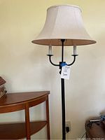 Full front view of the black metal floor lamp with tan oval shade showing the three bulb holders and fabric shade.