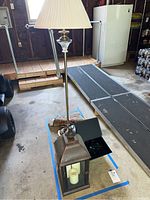 Photo of a brass floor lamp with fabric shade and a brown metal lantern with white pillar candles inside.