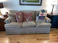 Front view of tan fabric sofa with four decorative pillows and a quilt draped on one arm.