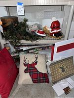 Holiday pillows, Santa figurine, pine cone garland, gift boxes, and wrapping paper under shelving unit