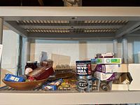Shelf with assorted items including boxes of plastic silverware, boxed mousetraps, cans of NEVR-DULL polish, zinnia growing kit, and other small items.