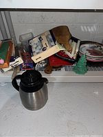 Wide shot of shelf showing coffee carafe, tea lights, plates, cutting board, dishes, and decor items