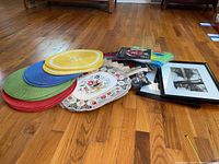 Photo showing colorful placemats stacked together with two framed pictures lying on wooden floor.
