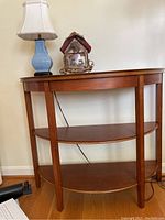 Full view of the half round wooden table with the lamp and bird house decor on top, showing the table shape and shelves.