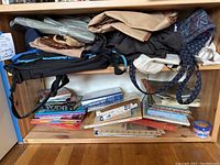 Shelf with assorted bags on top and stacked books on lower shelves