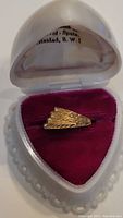 Front view of the gold ring inside a heart-shaped white case with burgundy velvet interior, showing the stepped design on top of the band.