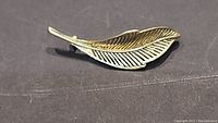 Front view of gold leaf-shaped brooch showing detailed vein pattern and curved stem design.
