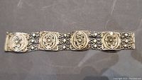 Full view of the antique sterling silver bracelet lying flat showing all five ornate panels connected by triple chain strands with spherical beads.