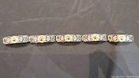 Full view of antique sterling silver bracelet laid flat on dark surface showing all joined segments with colorful micro mosaic floral patterns.