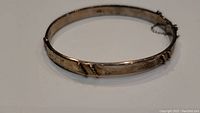 Overall front and side view of oval sterling silver bracelet showing engraved design and shape.