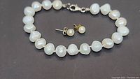 Full view of pearl bracelet and matching pearl stud earrings laid flat on dark surface.