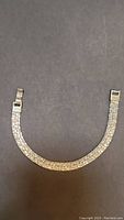 Full length of silver textured bracelet with fold-over clasp, laid flat on dark background