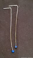 Full view of two silver chain earrings with blue beads on a black background.