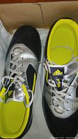 Pair of Adidas soccer shoes showing the left shoe top view displaying black and silver upper with yellow inner sole and lace closure