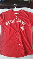 Front view of the red Toronto Blue Jays baseball jersey with white Blue Jays logo and text on front.