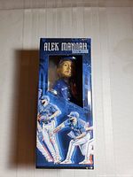 Front view of boxed Alek Manoah bobblehead with clear window showing the figure inside, blue-themed graphics with player action images and name.